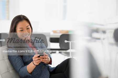 Business. A Woman Seated In A Comfortable Chair, Checking Her Smart Phone For Messages.