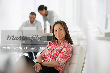 Business. A Woman Seated On The Sofa Looking Relaxed. Two People Working Together Looking At A Laptop.