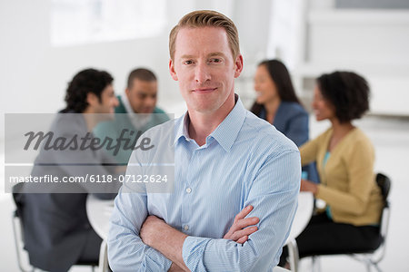 Business Meeting. A Group Sitting Down Around A Table. A Man Smiling Confidently.