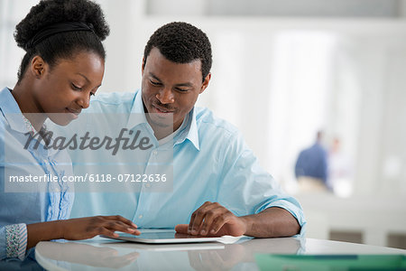 Office Interior. A Man And Woman Sitting Side By Side Using A Digital Tablet.