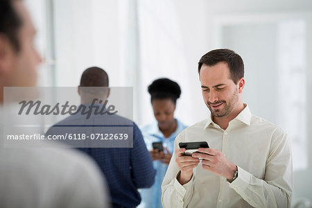 Office Interior. A Group Of People, One Man Using A Smart Phone.