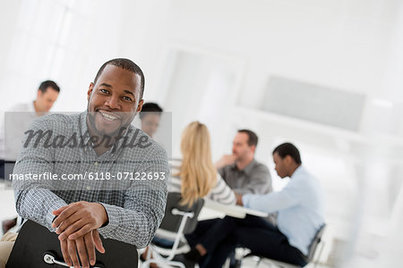 Office Interior. A Man Seated Separately From A Group Of People Seated Around A Table. A Business Meeting. Office Interior. A Man Seated Separately From A Group Of People Seated Around A Table. A Business Meeting.