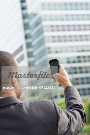 City. A Man In A Business Suit Holding His Smart Phone At Arms Length.