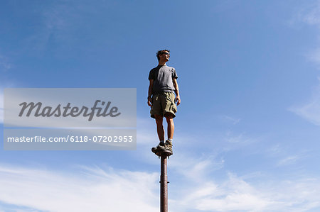 Man standing and balancing on a metal post, looking towards expansive sky, Surprise Mountain, Alpine Lakes Wilderness, Mt. Baker-Snoqualmie National forest.