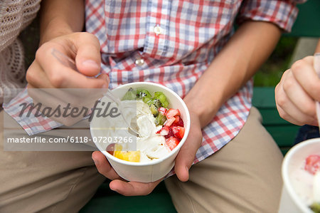 Young people sitting side by side, eating fresh organic fruit and yoghurt desert.