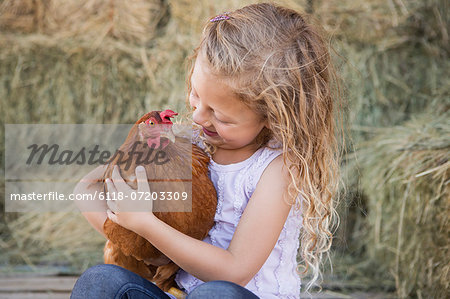 A young girl holding a chicken in a henhouse.