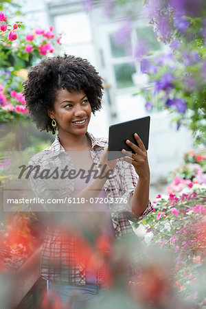 A woman in a plant nursery surrounded by flowering plants and green foliage. A woman in a plant nursery surrounded by flowering plants and green foliage.