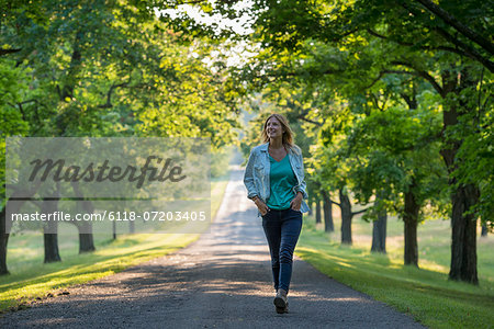 A woman walking down a tree lined path.