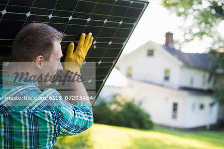 A man carrying a solar panel towards a building under construction.