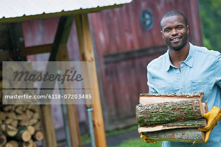 A young man carrying a pile of logs in from the logstore. Farm life.