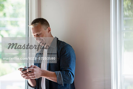 A man standing in a quiet corner of a cafe, using a smart phone.