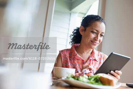 A young woman reading from the screen of a digital tablet, seated at a table. Coffee and a sandwich.