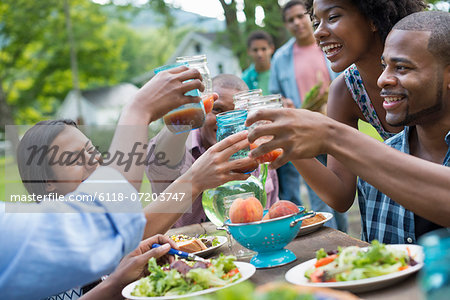 A group of adults and young people at a meal in the garden of a farmhouse. Passing plates and raising glasses.