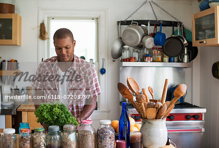 A young man in a kitchen preparing salad leaves and vegetables.