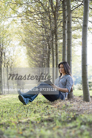 A woman sitting reading a book under the trees.