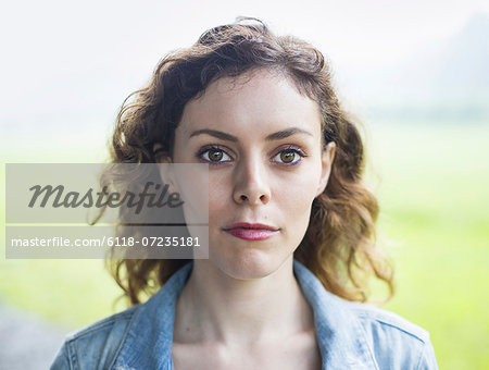 A young woman in a rural landscape, with windblown curly hair.