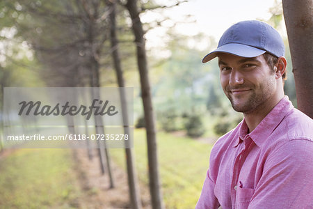 A man leaning against a tree, looking at the camera.