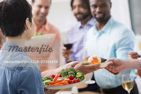 An open plan office in New York City. A working lunch, a salad buffet. A group of men and women of mixed ages and ethnicities meeting together.