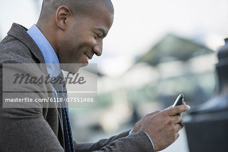 Business people in the city. Keeping in touch on the move. A man seated on a bench, checking his smart phone.