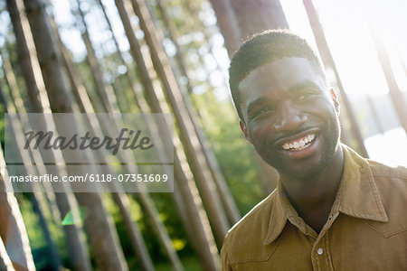 A man smiling at the camera under the shade of trees in summer.