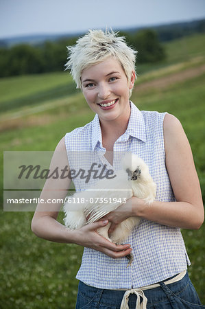 A young girl, teenager, holding a chicken with white feathers in her arms.