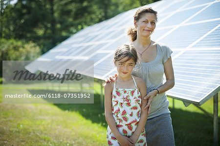 A child and her mother in the fresh open air, beside solar panels on a sunny day at a farm in New York State, USA.