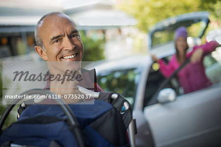 A man with a bag and a woman standing by the open car door, leaving for a trip.