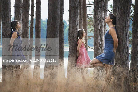 A group of people communing with nature, and leaning against tall straight trees in woodland.