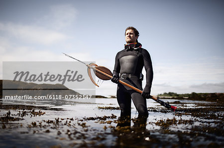 A man in a wetsuit, standing on the shore with a large spear fishing harpoon.  - Stock Photo - Masterfile - Premium Royalty-Free, Code: 6118-07352147