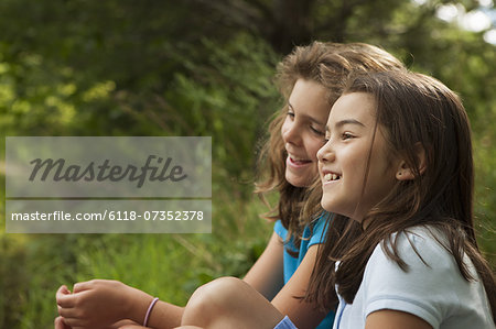 Two children, girls sitting side by side, laughing in the fresh air.