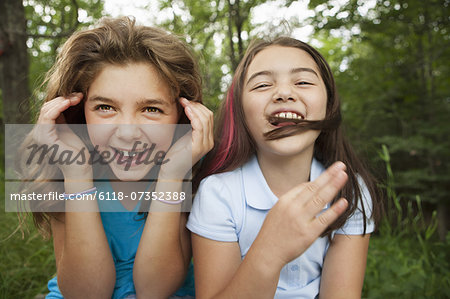Two girls, friends sitting side by side, playing and laughing.