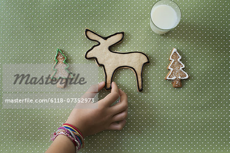 A girl's hand arranging an organic homemade Christmas cookies in the shape of a reindeer and Christmas trees.