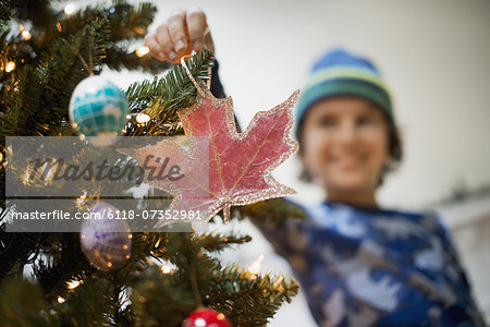 A young boy holding Christmas ornaments and placing them on the Christmas tree.