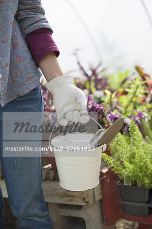 A woman carrying a white tin bucket with gardening tools, on an organic farm.
