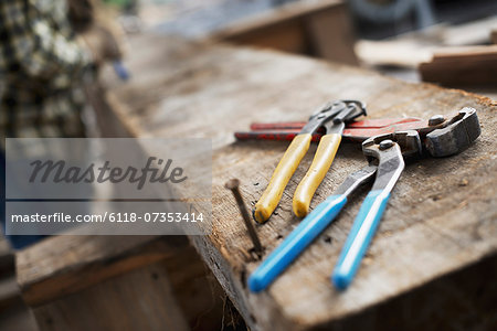 A reclaimed lumber workshop. A person at a workbench, and tools, grippers and pliers lined up on a plank of wood.
