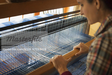 A woman seated at a wooden handloom creating a handwoven woollen fabric, with a blue and white pattern.