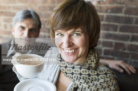 Two people sitting in a coffee shop. A man and woman, holding white china cups of cappuccino coffee.