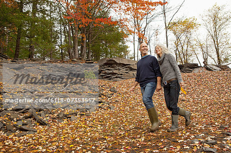 A couple, man and woman on a day out in autumn walking through fallen leaves. Holding hands.