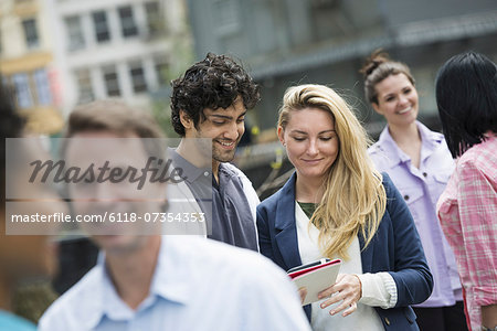 People outdoors in the city in spring time. New York City. A group of men and women, a couple at the centre looking at a cell phone.