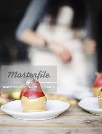 A woman in a domestic kitchen. Fresh organic pears dipped into a sauce for dessert laid out on plates.