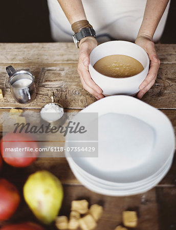 A domestic kitchen tabletop. A stack of white plates and fresh pears and a stack of sugar cubes. A bowl of  fudge sauce.