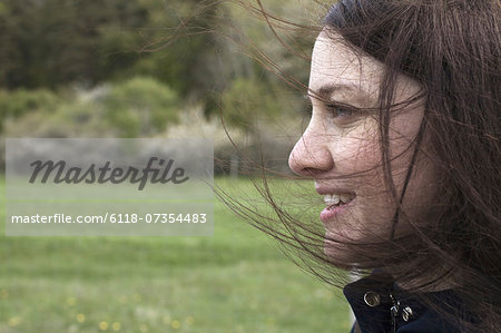 A young woman in profile. Her brown hair blowing about her face. Outdoors. Spring.