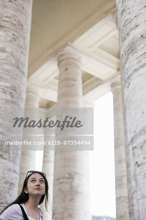 A woman looking up at the tall pillars and arches of a historic building in Rome.