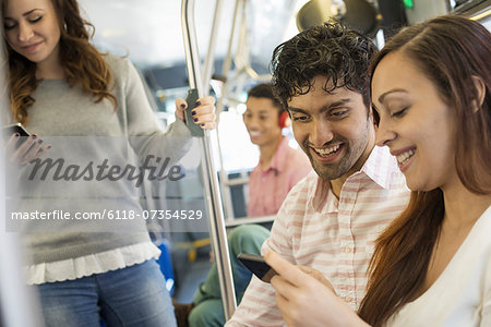 Urban Lifestyle. A group of people, men and women on a city bus, in New York city. A man wearing headphones and a couple looking at a mobile phone.