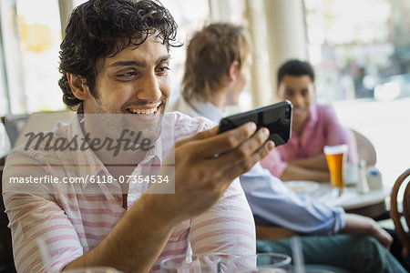 Urban Lifestyle. Three young men around a table in a cafe. One using his smart phone