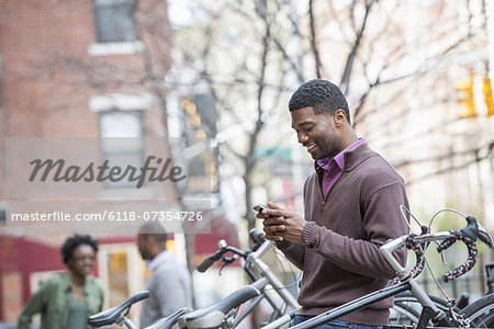 Outdoors in the city in spring. An urban lifestyle. A young man checking his phone and texting. Cycle rack and stored bicycles.