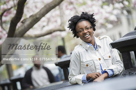 Outdoors in the city in spring. An urban lifestyle. A woman seated at a table with two men in the background.