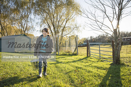A young boy in an animal paddock, holding a bucket of feed. Animal sanctuary.