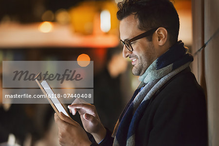A man in a city at night, looking at a computer tablet.
