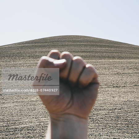 A hand bunched up and making fist, making a gesture. A ploughed field and farmland in the background, near Pullman in Washington state.